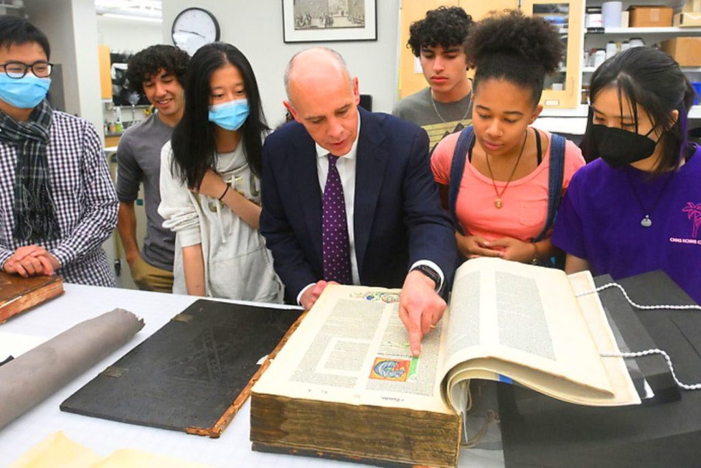 Dean Chris Celenza reading through a large format book with 7-8 students