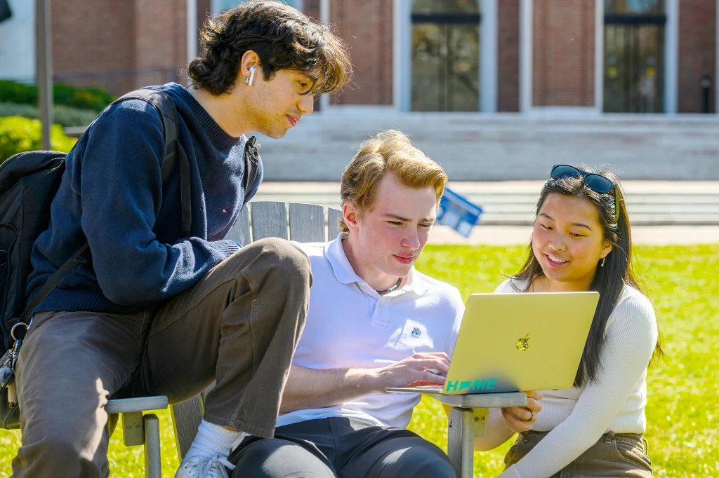three students looking at a laptop screen outdoors on Homewood campus on a sunny day