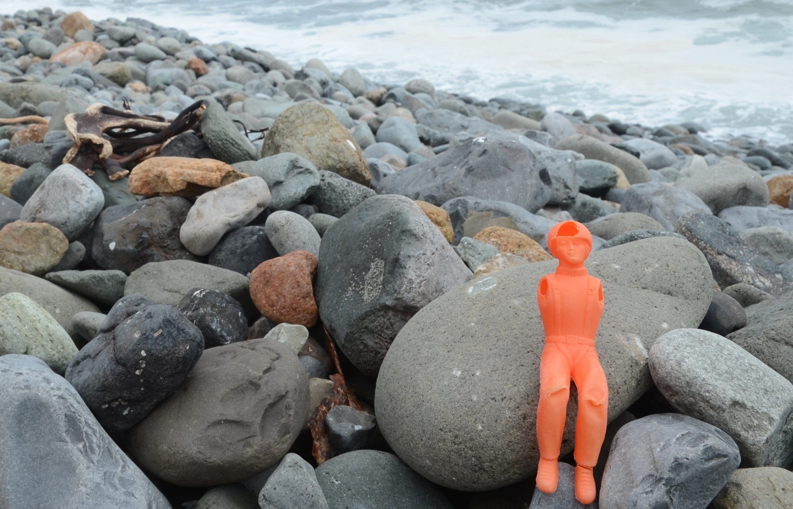 orange plastic man sitting on rocks on the shore