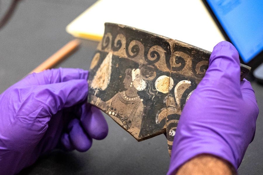 Close-up view of students hands holding pottery shard during class in the JHU Archaeological Museum.