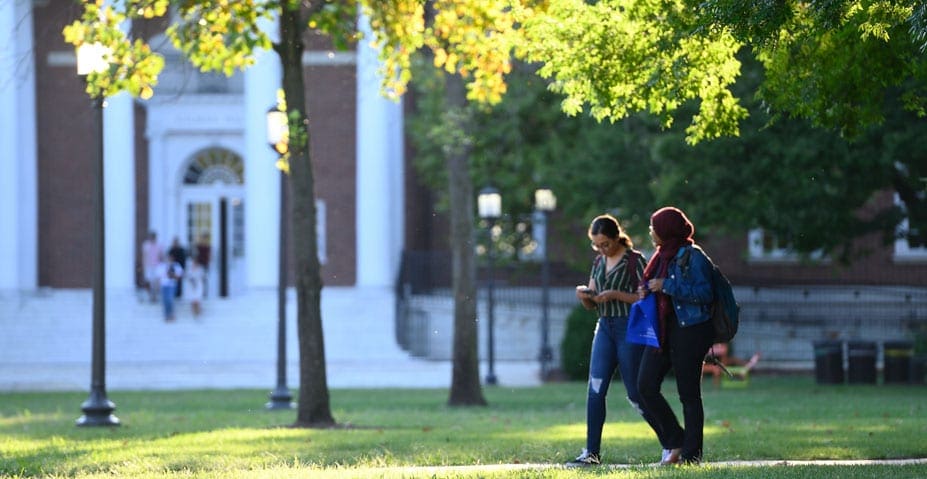 two students walking on campus in front of Gilman Hall