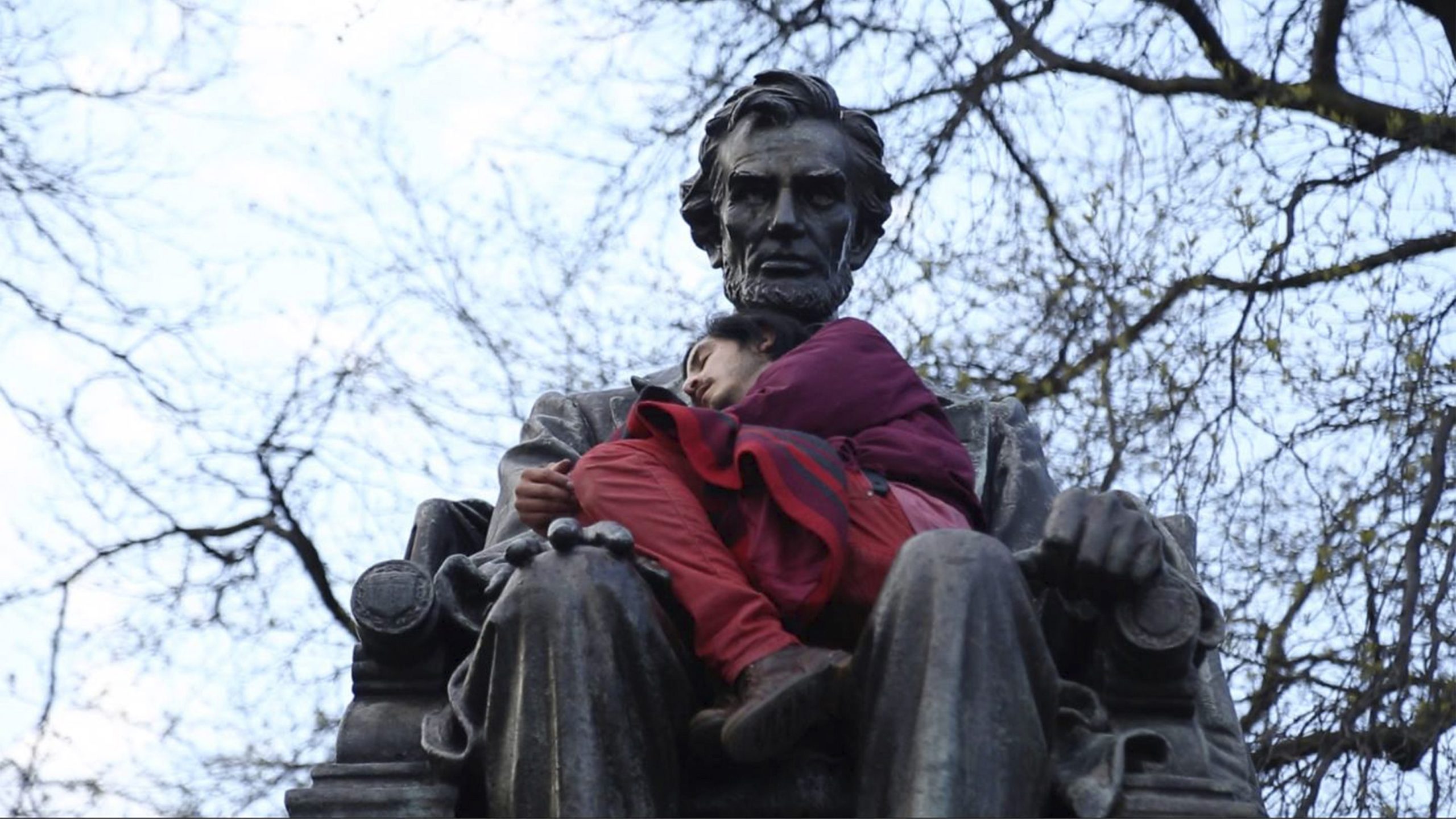 photo of a man sleeping in the arms of a statue of Abraham Lincoln.