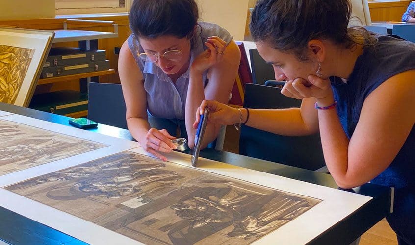 two women looking closely at lithograph print