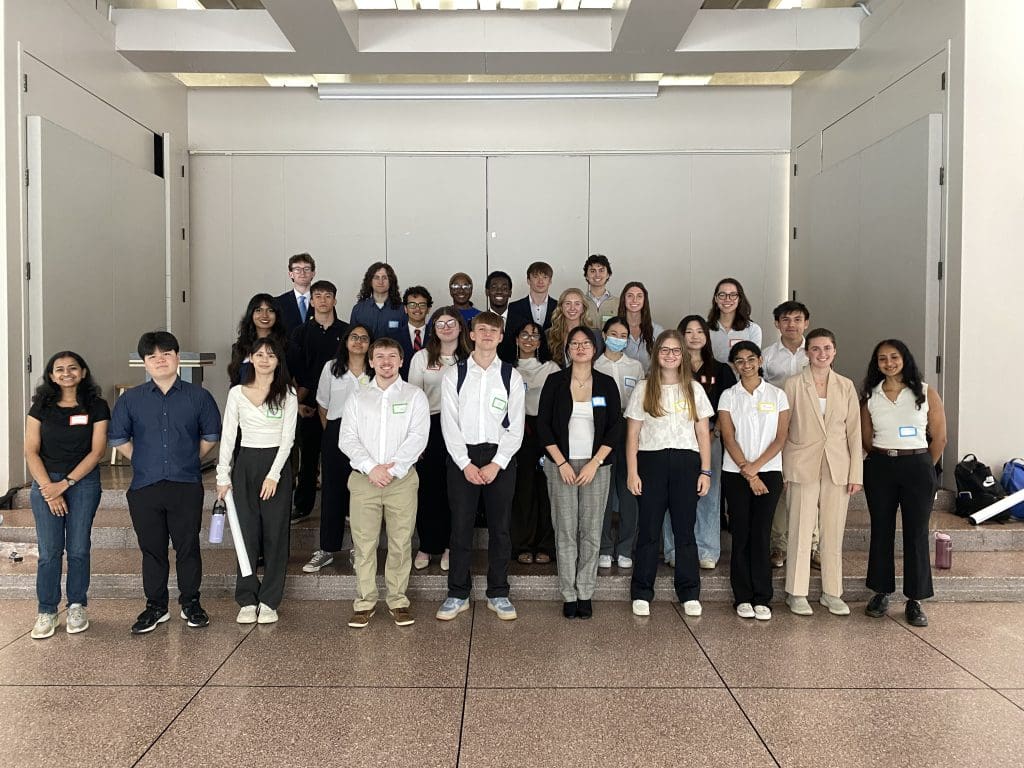 students in business casual attire smile at the camera after presenting their posters