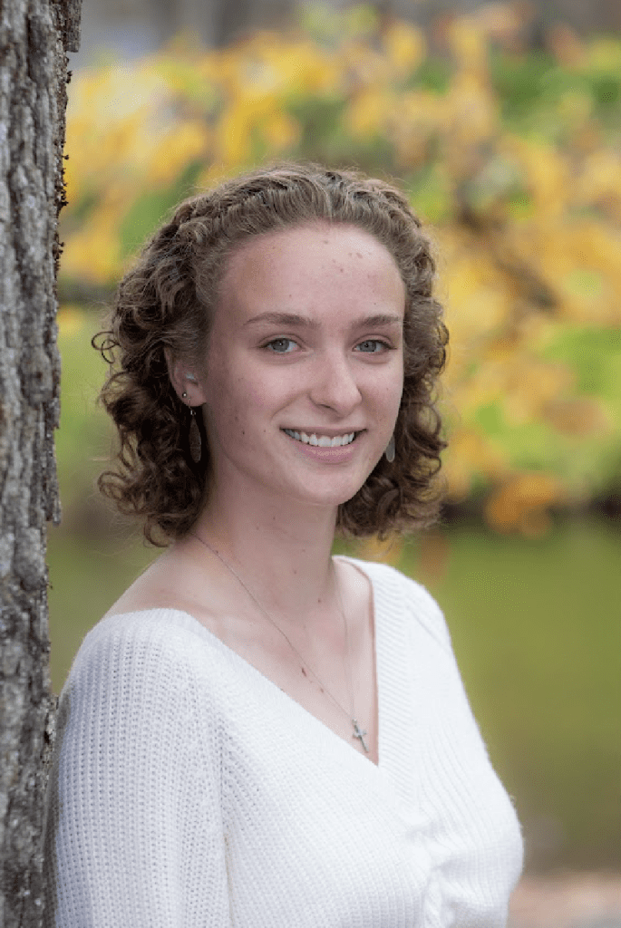 Addison smiling in a white blouse with her back to a tree