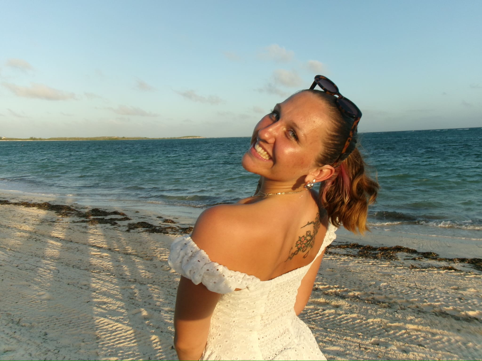 greta smiling and looking over her shoulder in a white dress on the beach