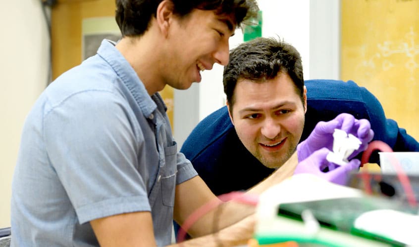 Chemistry professor Stephen Fried (r) and student looking at samples in small containers.