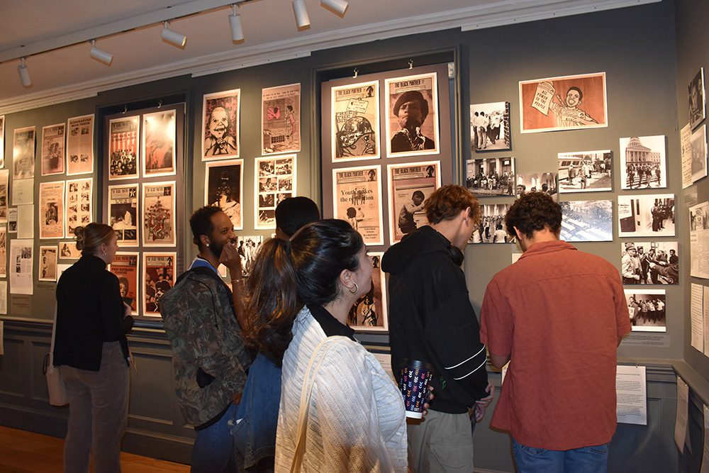 group of people standing in a museum exhibit with posters and newspaper clippings on the wall