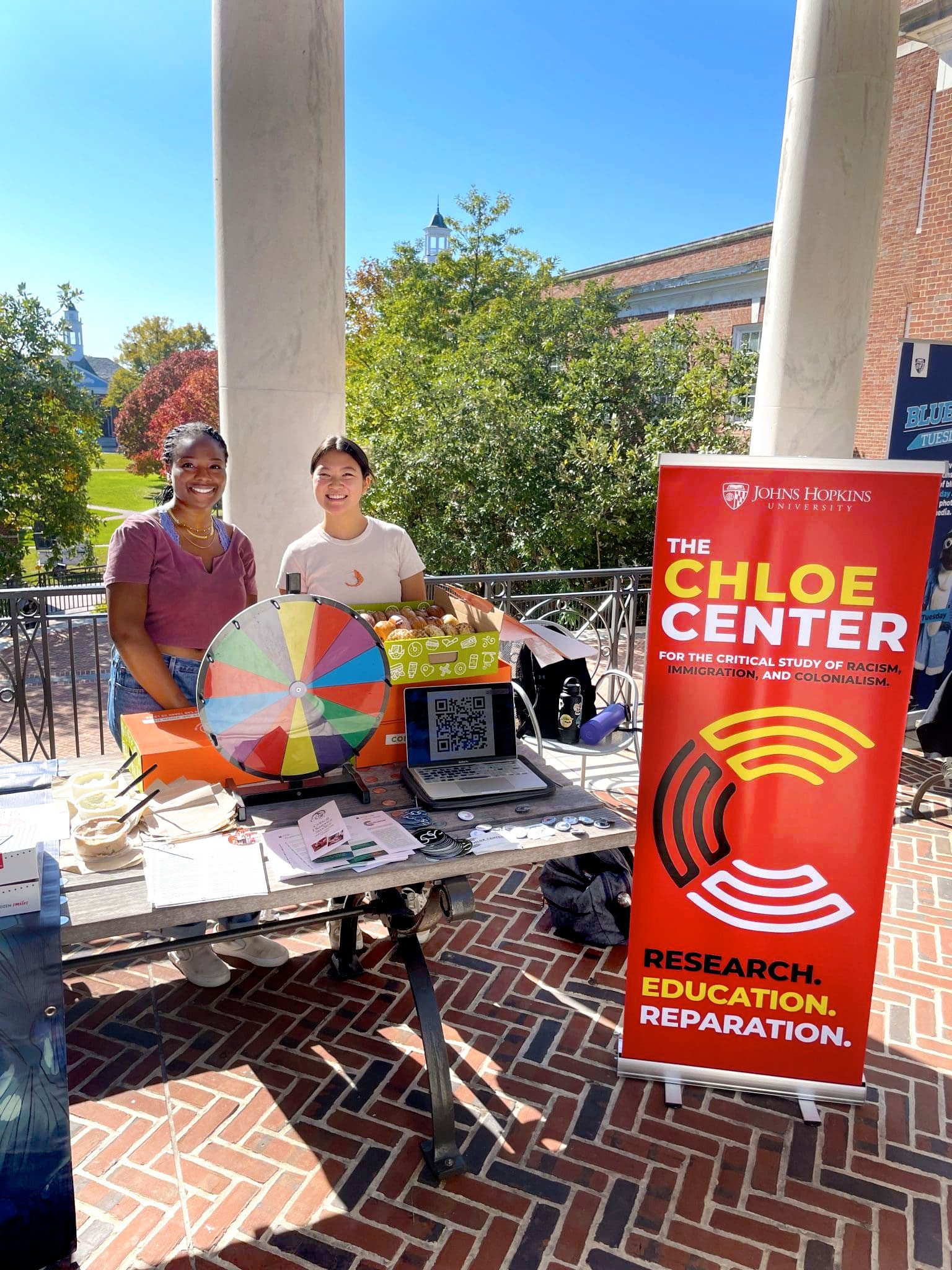 Two students stand at a table with the Chloe Center banner, handing out information about the CDS major