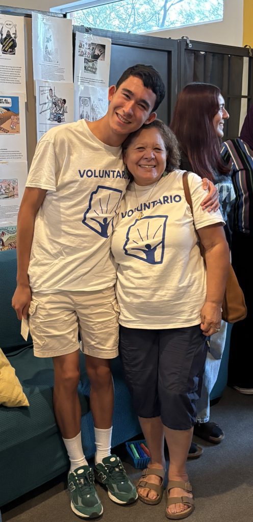 Young student with older woman, both wearing the same shirt that reads Voluntario.