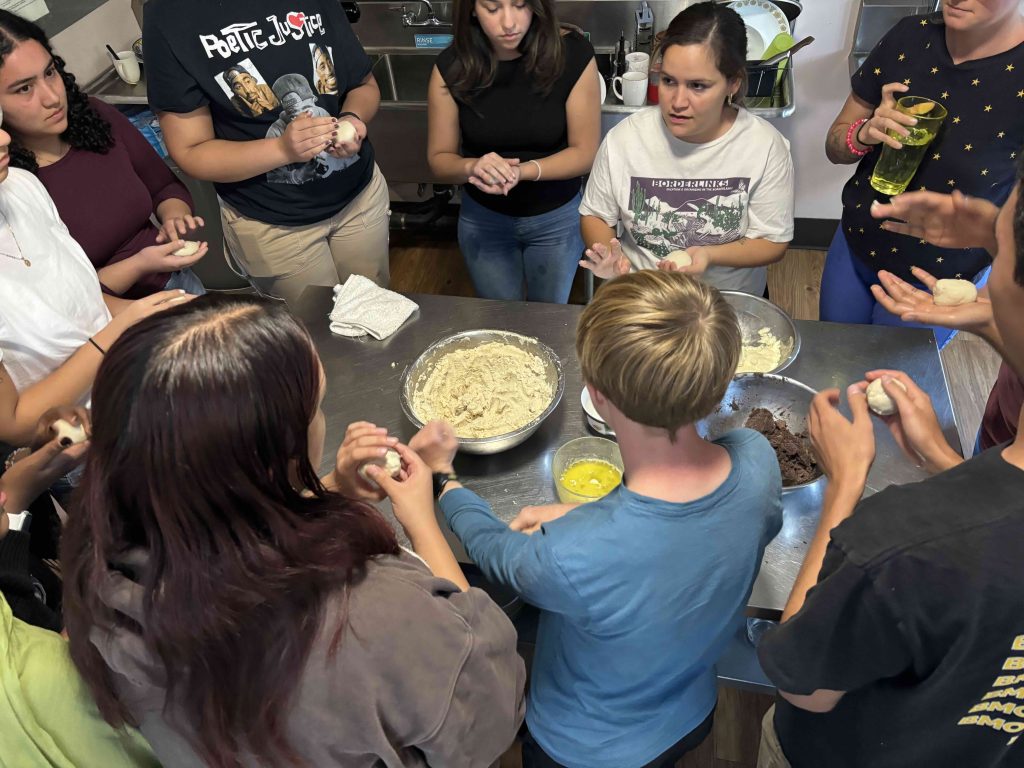 Students and staff stand around counter with pupusa ingredients.