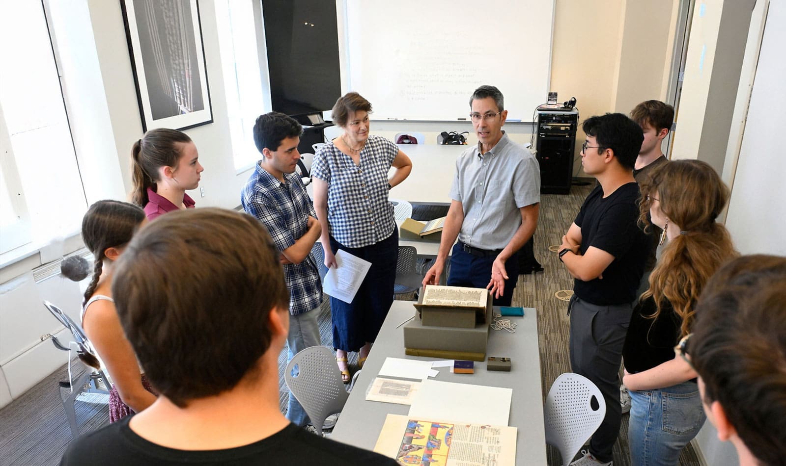 Faculty (Chris Cannon) discussing with students while holding a antique book.