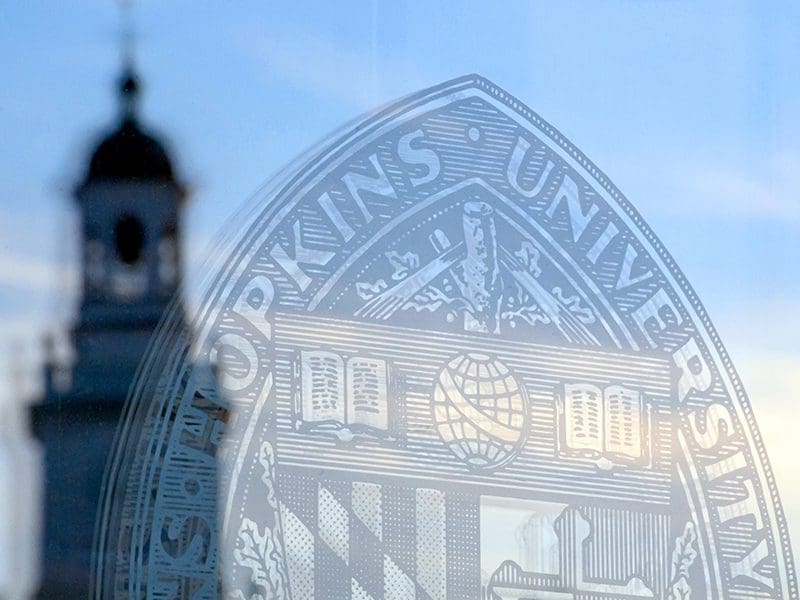 Hopkins shield etched in glass with Gilman tower in the background.