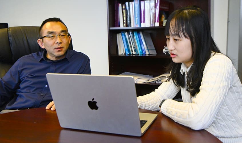 Professor Yingyao Hu with student looking at laptop in his office.