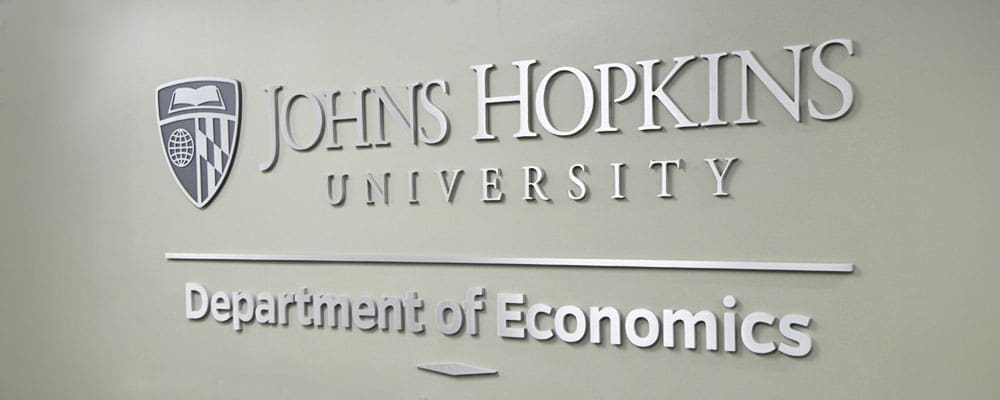 "Department of Economics" signage in the foyer with the Johns Hopkins logo displayed in raised letters.