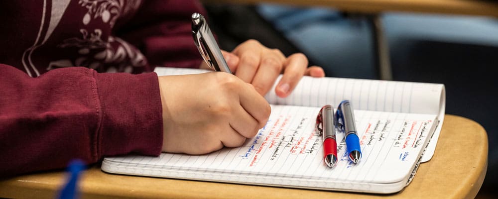 Closeup of undergraduate student's hands taking notes on paper with blue and red pens.