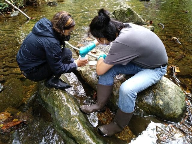 two students wearing gloves and boots pulling samples in a stream