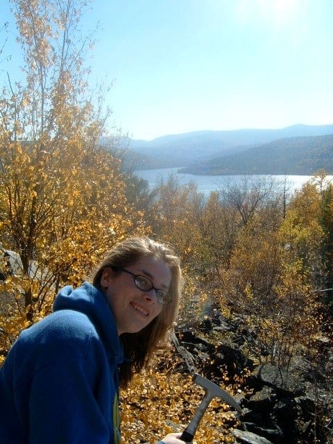 person with long hair standing above a river and trees with yellow leaves