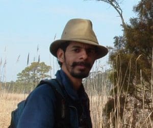 Person with a beard and brimmed hat in a field