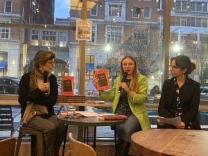 Panel of Ann Goldstein, Marta Cerreti, and Cristina D'Errico seated on stools at front of bookstore in evening.