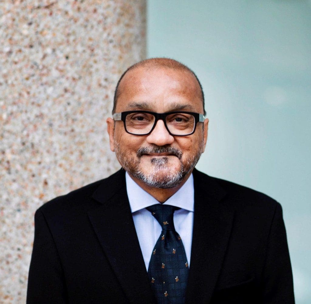 Headshot of Aamir Mufti, a smiling man wearing a suit and tie and eyeglasses