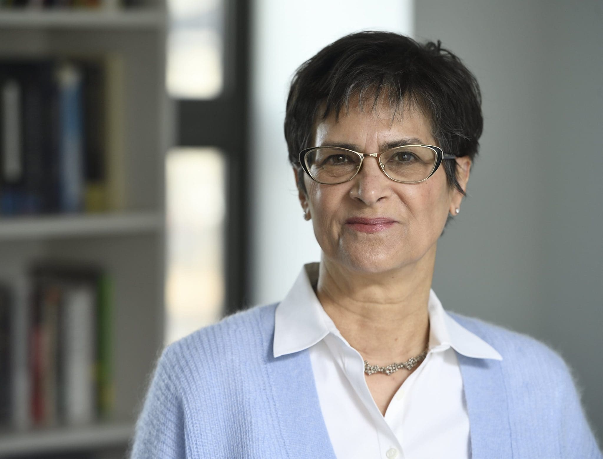 Martha S. Jones standing in front on a bookcase, wearing eye glasses, a white collar shirt and a periwinkle sweater