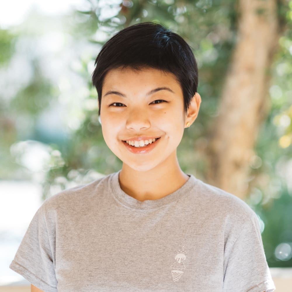 Myra Cheng smiling wearing a grey t-shirt with trees in the background