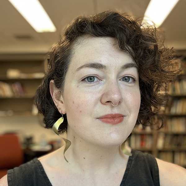 Headshot of Alessandra Amin, a woman with curly hair and spiral earrings