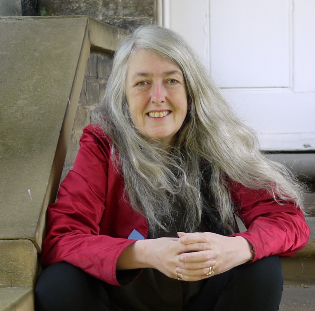 Mary Beard sitting on steps, hands folded, wearing red top