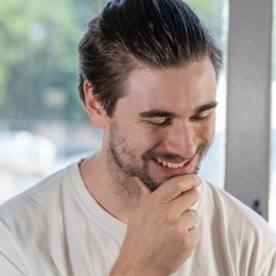 Photo of Dr. Milan Terlunen, hand on chin, smiling, and looking down