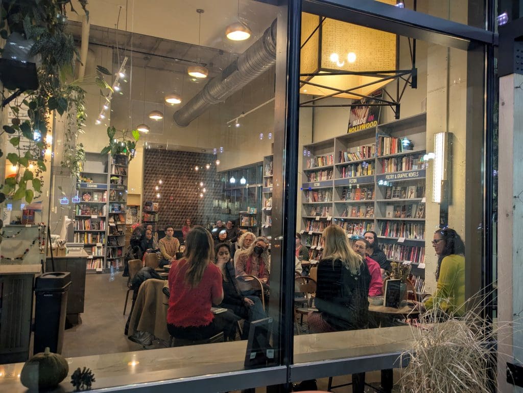 Photo from outside of Bird in Hand window showing folks seated and listening to the conversation 