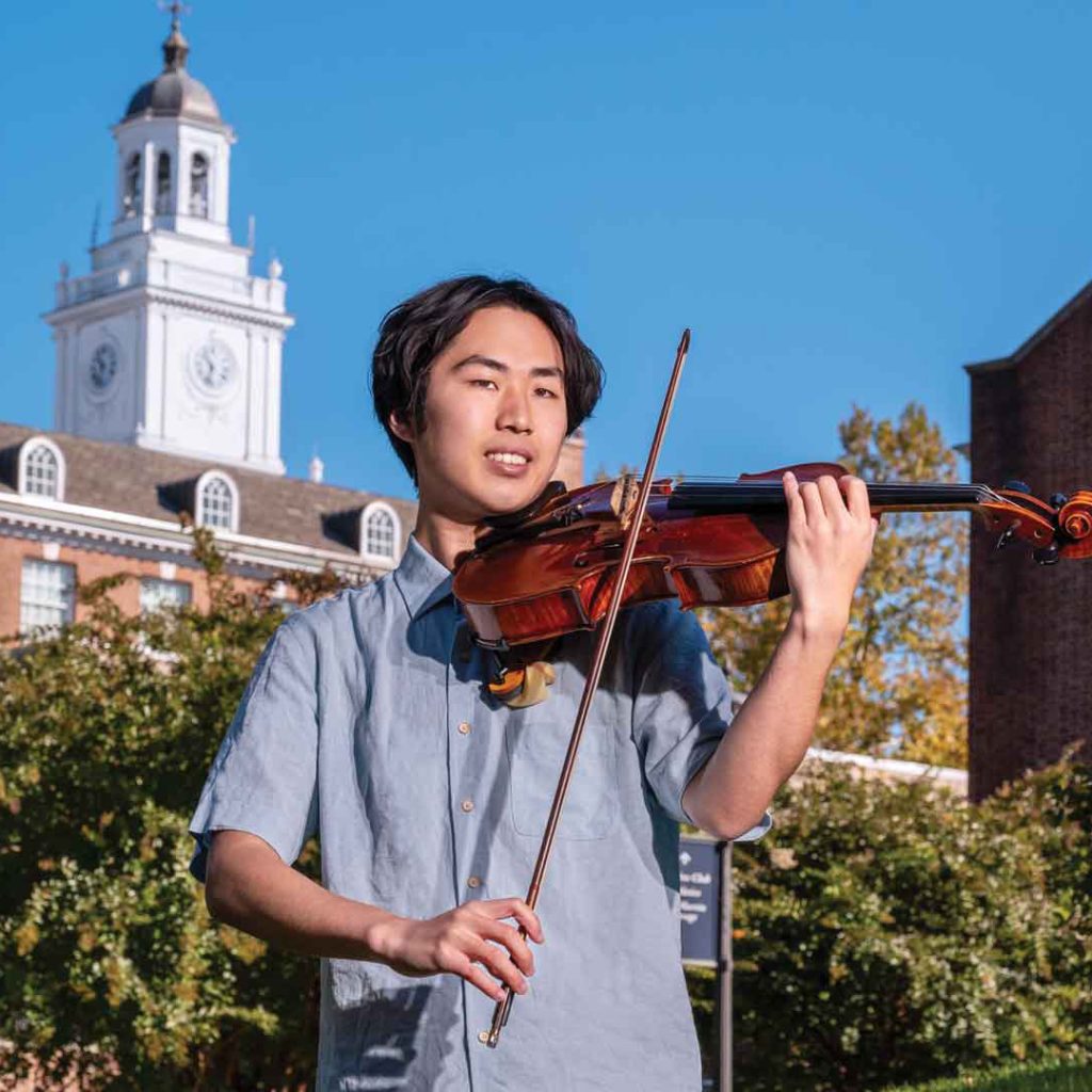 Henry Hung playing a viola in front of a Johns Hopkins brick building