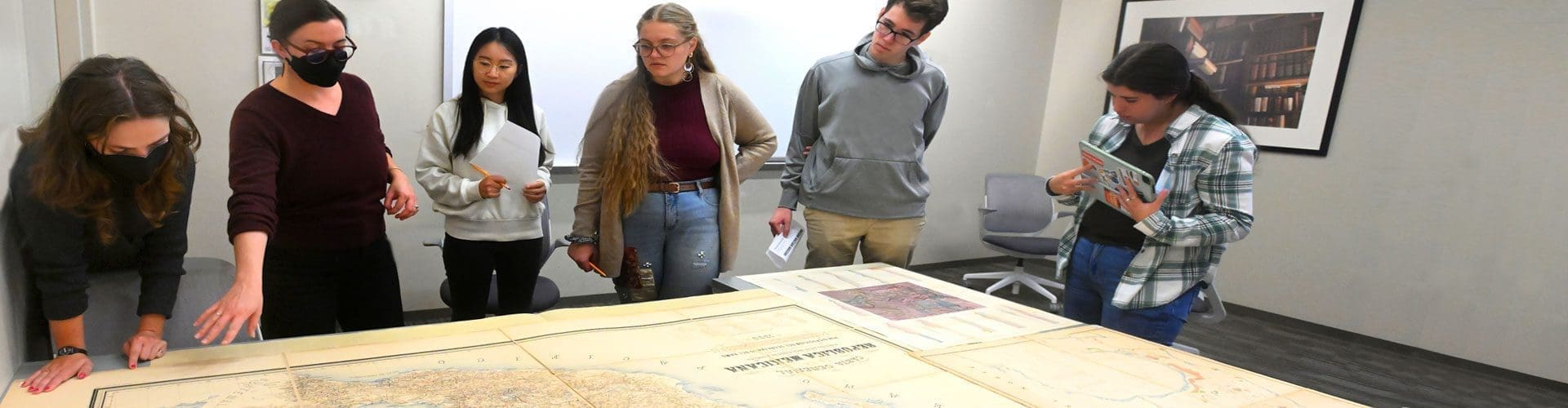 Prof. Casey Lurtz gestures at a table sized map of Mexico from the 19th Century while five students examine it.