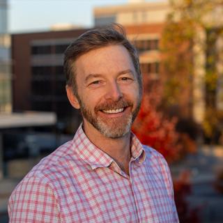 Dr. Conway is turned slightly to right of image and is smiling facing the camera wearing a red and white plaid shirt.