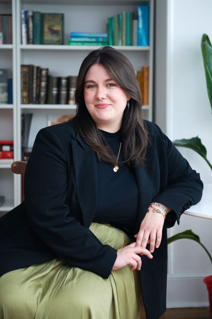 White woman sitting in chair in front of bookshelves