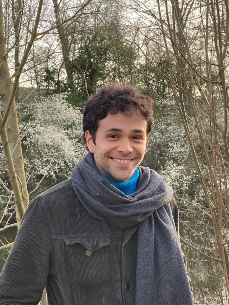 man with scarf in front of snowy trees