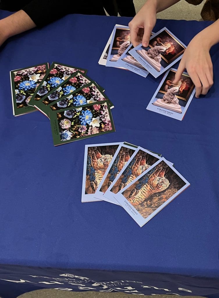 Groups of postcards showing artworks lie on a table. Hands appear in the photo picking up one group of postcards