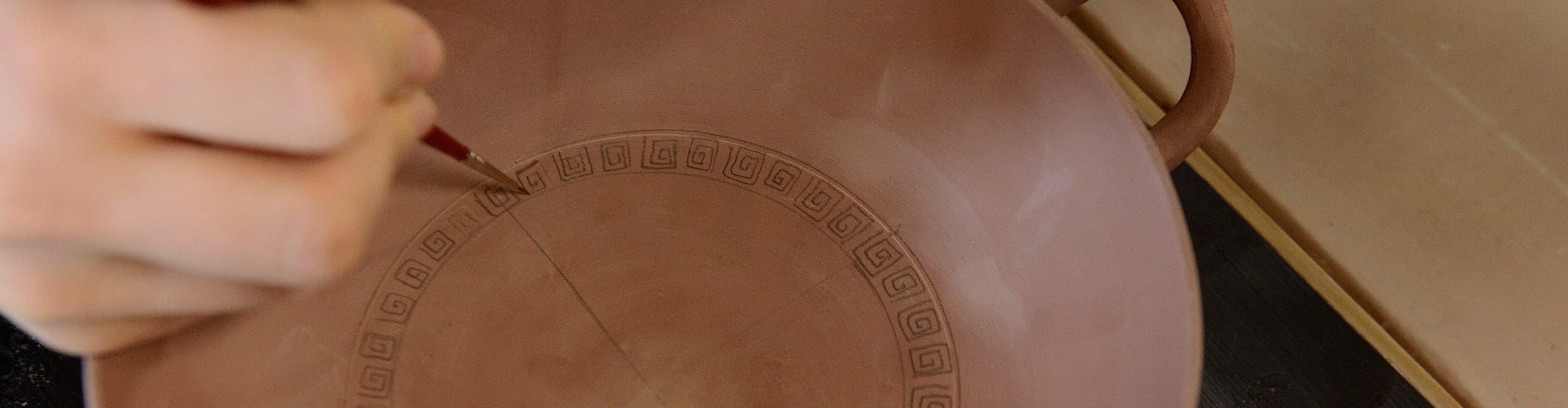 close-up photo of student's hand painting kylix (drinking bowl)