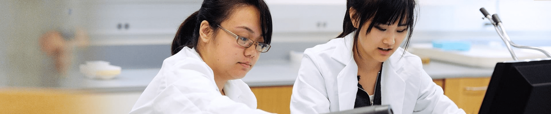 two female students wearing white lab coats working in the lab