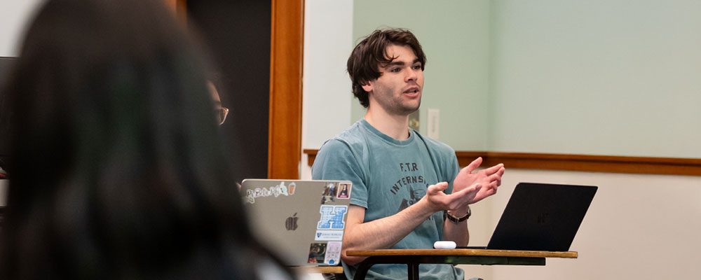 Student discussing in class while sitting at a desk.