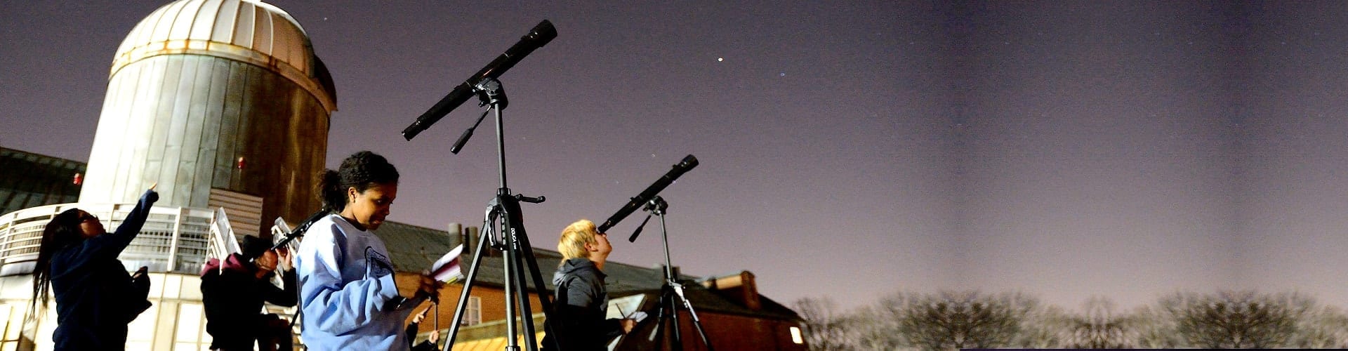 several students with telescopes on a roof at night looking at stars
