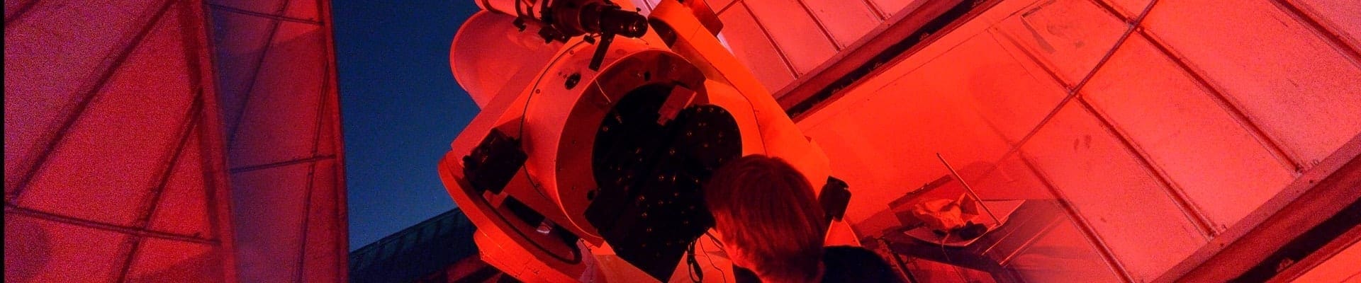 person at a huge telescope in a red-lit room