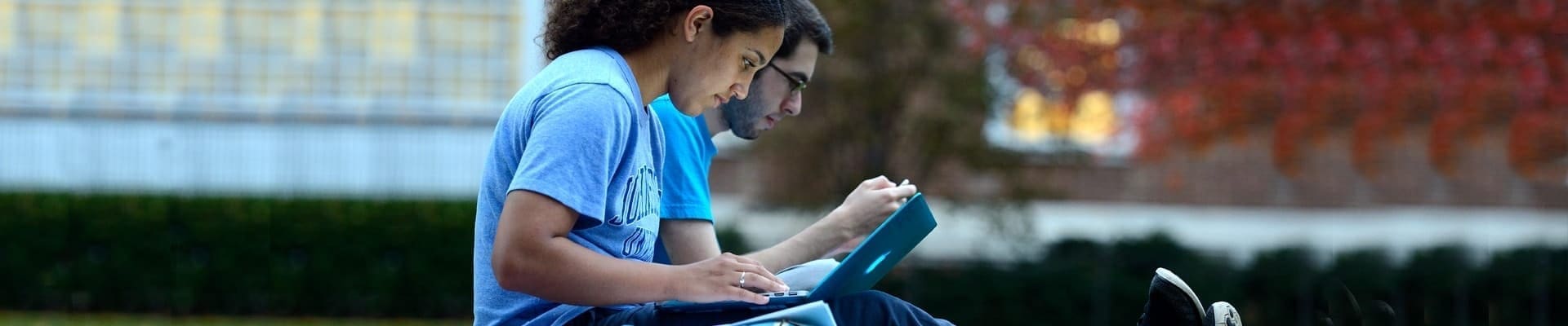 Two students outside on a lawn with laptops on their laps
