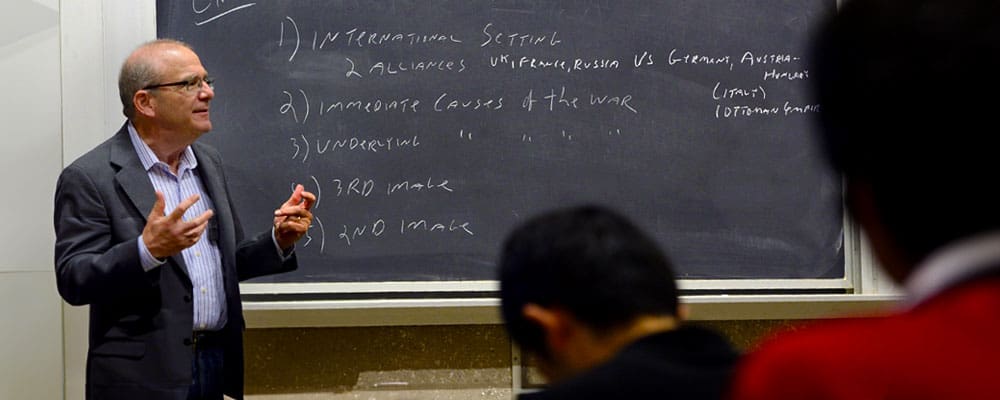 Professor Steven David lectures undergraduates in front of a blackboard with bullet points about war and alliances.