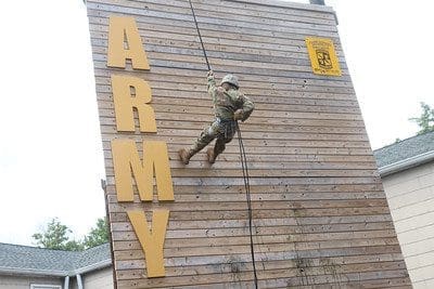 Cadet in fatigues repelling down wooden wall with ARMY on the left