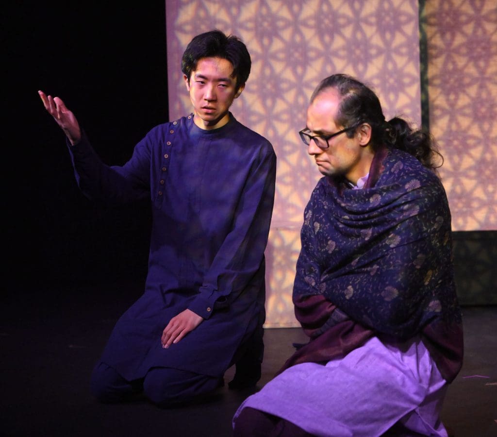 Two people kneel in a temple, in discussion.