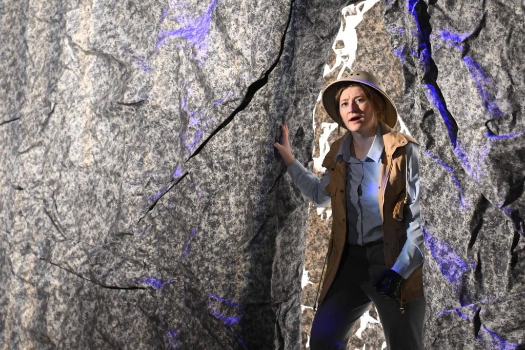 A hiker, in a pith helmet, walks through a cave.