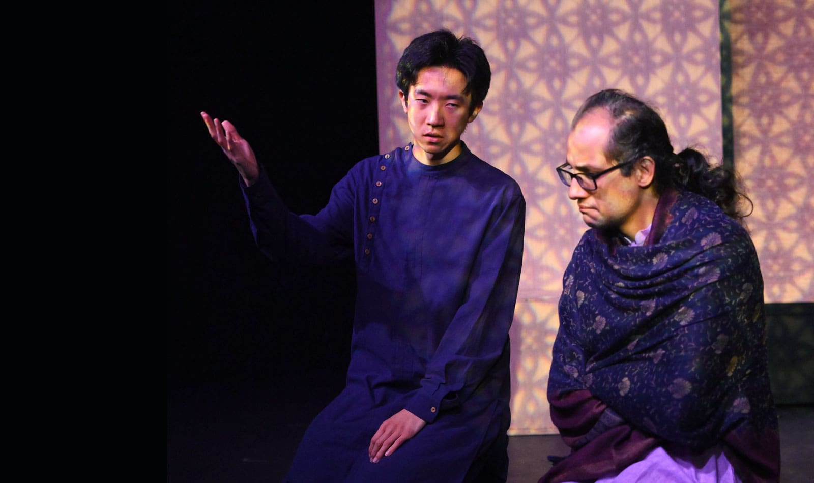 Two people kneel in a temple, in discussion.