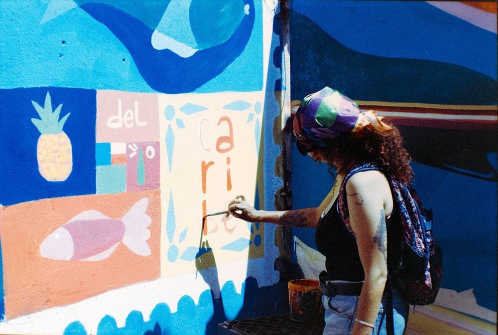 A person with a ponytail painting orange and yellow patterns on a blue wall