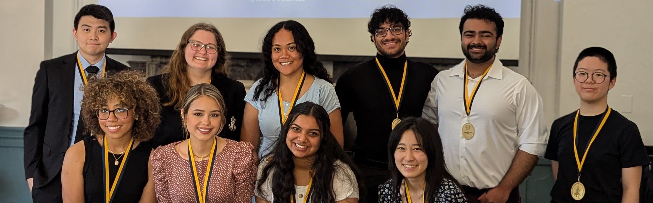 Ten students stand together in the Great Hall wearing the medals they earned for completing the University Undergraduate Research Fellowship.